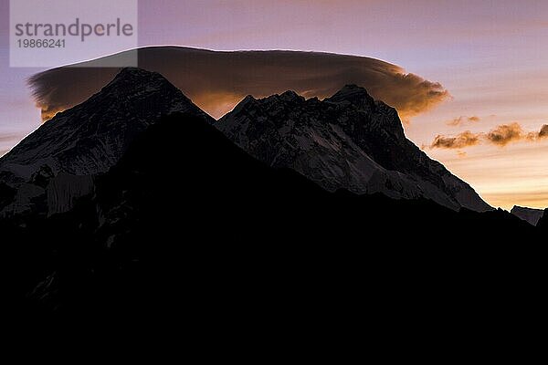 Die Silhouetten der beiden Achttausender Mount Everest und Lhotse im Gegenlicht der aufgehenden Sonne  mit einer linsenförmigen Wolke über den Gipfeln. Gesehen vom Gipfel des Gokyo Ri  dem beliebten Trekking Gipfel in der Everest Region  in der Morgendämmerung eines Novembertages. Herbst  Nachmonsun Trekking Saison. Gokyo Trek  Khumbu  Everest Region  Himalaya. Der Sagarmatha Nationalpark  ein UNESCO Weltnaturerbe. Solukhumbu  Nepal  Asien