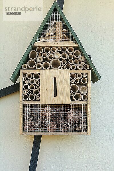 Nahaufnahme einer Vorderansicht eines aufwändig gestalteten Insektenhotels mit grünem Spitze Dach  mit Abschnitten von Tannenzapfen und kreisförmige Holzstücke.  Close up front view of intricately designed wooden bird table with green apex roof  with sections of pine cones and cClose up front view of intricately designed wooden bird table with green apex roof  with sections of pine cones and cirular pieces of wood