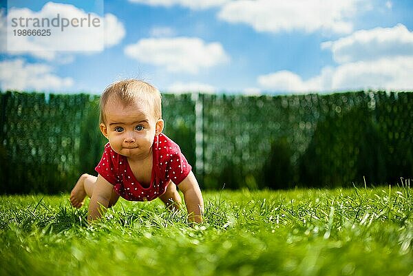 Nettes Baby auf allen Vieren in roten Körper auf grünem Gras mit blauem Himmel und Wolken