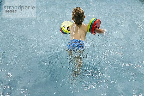 Thema: Vorschulkind beim Schwimmunterricht mit Schwimmflügeln in einem öffentlichen Bad