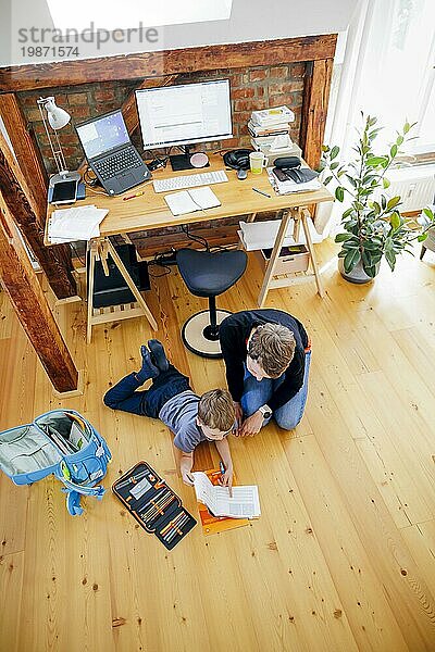 Staged shot: A six-year-old boy lies with his school bag next to his mother's desk and receives help with his homework. Berlin  08/08/2023