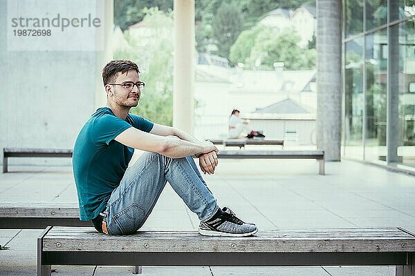 Männlicher junger Angestellter sitzt im Freien und macht eine Pause. Städtische Geschäftsumgebung