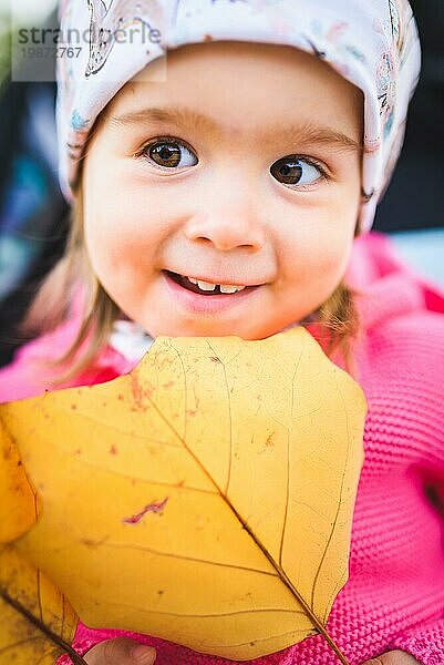 Porträt von adorable Baby Mädchen mit großen gelben Blatt im Herbst. Baby in der Natur Konzept