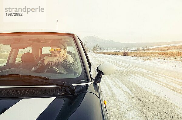 Hipster Frau mit Sonnenbrille sitzt in einem kleinen Auto im Winter