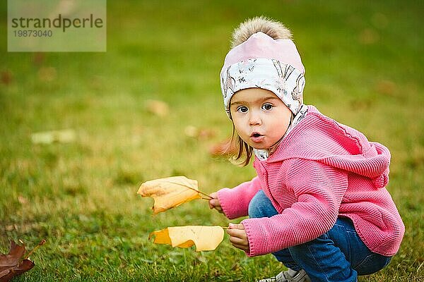 Porträt von adorable baby girl holding yellow leaves and ducking in autumn park. Baby in der Natur Konzept