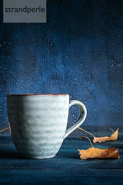 Herbstliche Stimmung. Eine Tasse Tee und Herbstblätter vor einem Fenster mit Regentropfen