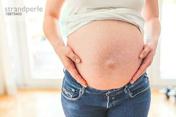 Glückliche kaukasische schwangere Mutter  die ihren nackten Bauch berührt  Blue Jeans  Nahaufnahme