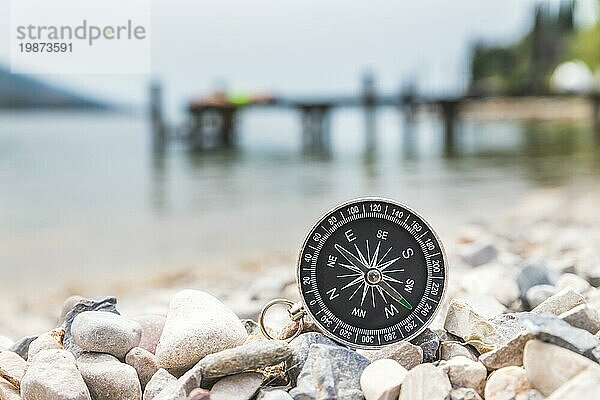 Nahaufnahme eines nautischen Kompasses am Strand  Küstenlinie im unscharfen Hintergrund