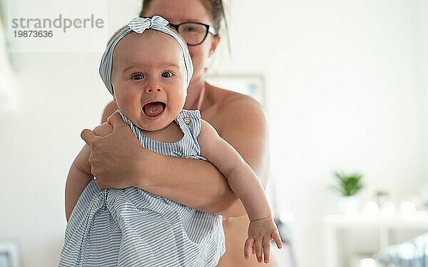 Junge Mutter hält lachendes kleines Mädchen. Heller Lifestylehintergrund