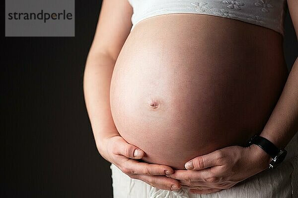 Bauch einer schwangeren Frau von der Seite. Dunkler Hintergrund  Kopierraum
