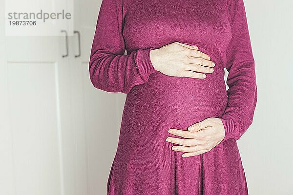 Nahaufnahme eines schwangeren Bauches  kaukasische Mutter im magentafarbenen Kleid