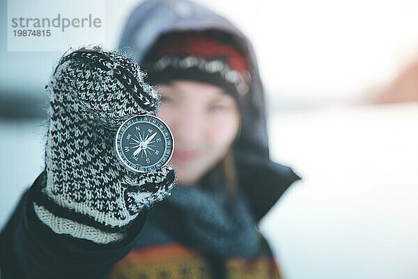 Junge lächelnde Frau hält einen Kompass hoch. Winterzeit  Handschuhe und Kapuze