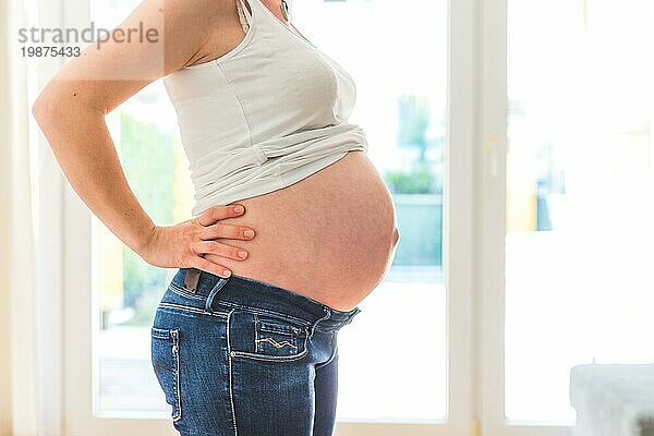 Glückliche kaukasische schwangere Mutter  die ihren nackten Bauch berührt  Blue Jeans  Nahaufnahme