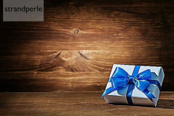 Weiße Geschenkbox mit blaür Schleife auf Vintage Holz