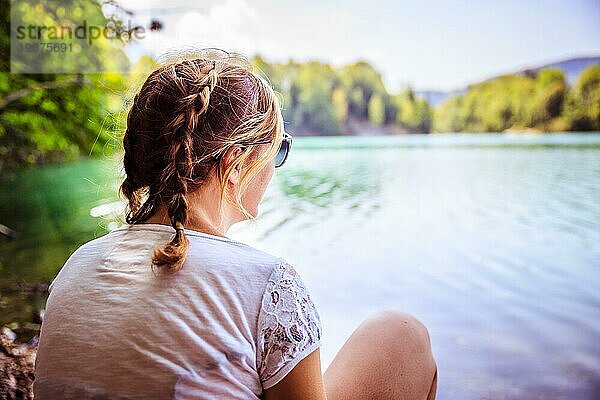 Schöne junge Frau sitzt an einem See und genießt den Tag