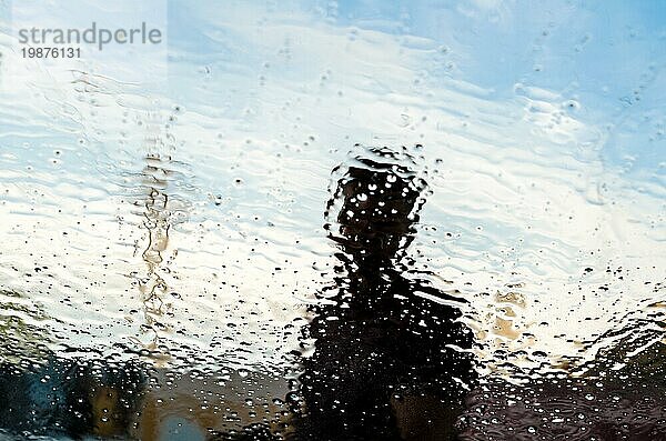 Autowaschanlage Wasser Textur auf Glas mit Mann hinter ihm auf einem blaün Himmel Hintergrund
