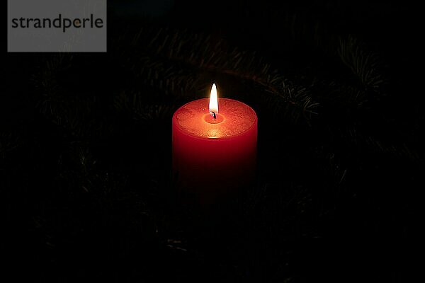 Weihnachtsmotiv mit rot brennender Kerze und schwarzem Hintergrund