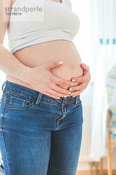 Kaukasische schwangere Mutter  die ihren nackten Bauch berührt  Blue Jeans  Nahaufnahme