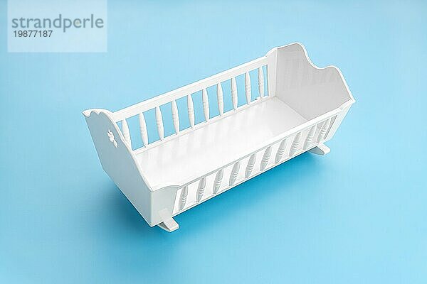 Weißes Babybettchen vorblauem Hintergrund. Kind Geburtenrate Konzept