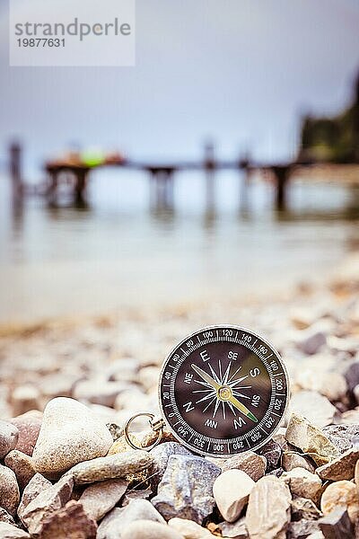 Nahaufnahme eines nautischen Kompasses am Strand  Küstenlinie im unscharfen Hintergrund