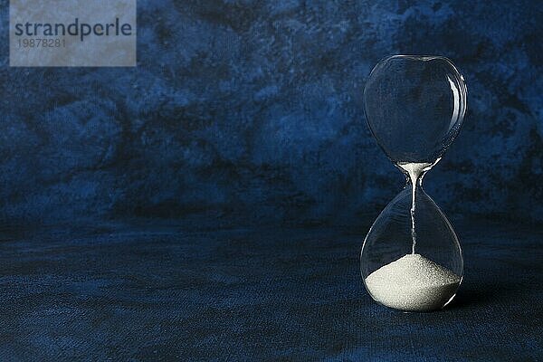 Die Zeit läuft ab Konzept. Eine Sanduhr mit sickerndem Sand  auf einem dunkelblauen Hintergrund mit Copyspace