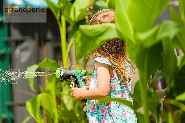 23 Jahre altes Mädchen mit Gartenschlauch Wasser die Pflanzen Pflanzen. Aktivität für Kinder im Sommer Konzept