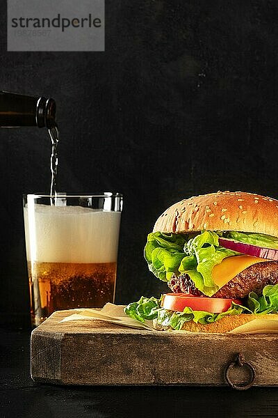 Burger und Bier. Hamburger mit Rindfleisch  Käse  Zwiebel  Tomate und grünem Salat  eine Seitenansicht auf einem dunklen Hintergrund mit Kopierraum. Selektiver Fokus