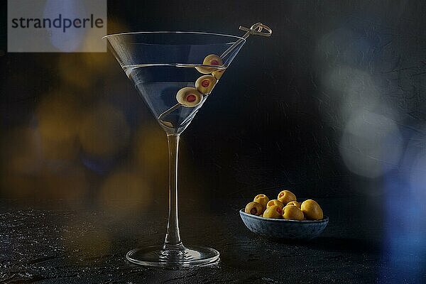 Martini  ein Glas mit würzigen Oliven  auf einem schwarzen Hintergrund. Alkoholisches Getränk mit Bokeh  getöntes Bild