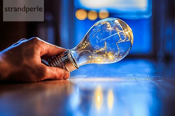 Die Hände halten eine LEDglühbirne über dem Holzboden. Symbol für Ideen und Innovation. Fenster und Licht im unscharfen Hintergrund