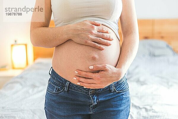 Kaukasische schwangere Mutter  die ihren nackten Bauch berührt  Blue Jeans  Nahaufnahme