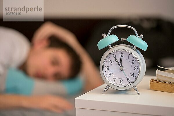 Weißer Wecker auf dem Nachttisch. Junger Mann schläft im Hintergrund