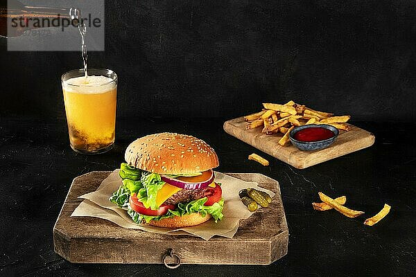 Burger und Bier. Hamburger mit Rindfleisch  Käse  Zwiebel  Tomate und grünem Salat  auf dunklem Hintergrund mit Kopierraum  Essiggurken und Pommes frites. Selektiver Fokus