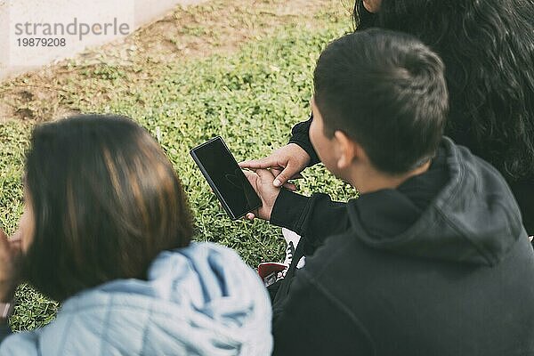 Drei Personen sitzen im Gras und schauen gemeinsam auf ein Tablet in einer zwanglosen Umgebung im Freien