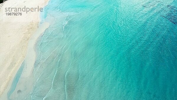 Luftaufnahme eines ruhigen türkisfarbenen Ozeans  der sanft an einen Sandstrand plätschert
