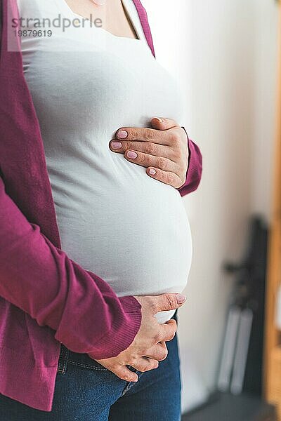 Nahaufnahme eines schwangeren Bauches  kaukasische Mutter mit weißem Hemd und magentafarbener Jacke