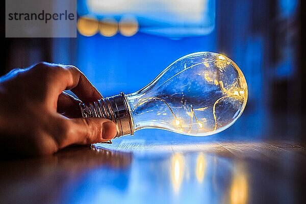 Die Hände halten eine LEDglühbirne über dem Holzboden. Symbol für Ideen und Innovation. Fenster und Licht im unscharfen Hintergrund