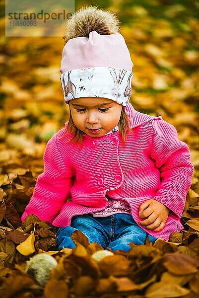 Baby Mädchen im Herbst Park sitzen in Haufen von trockenen Blättern Spaß haben. Eggenberg Park in Graz Österreich