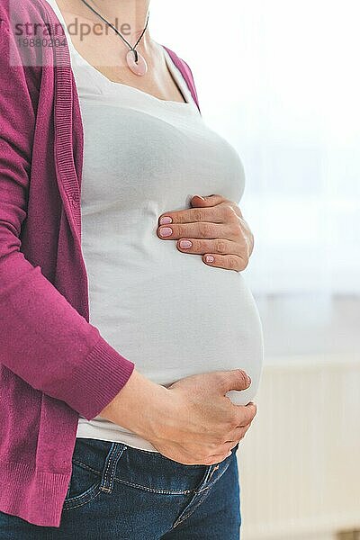 Nahaufnahme eines schwangeren Bauches  kaukasische Mutter mit weißem Hemd und magentafarbener Jacke