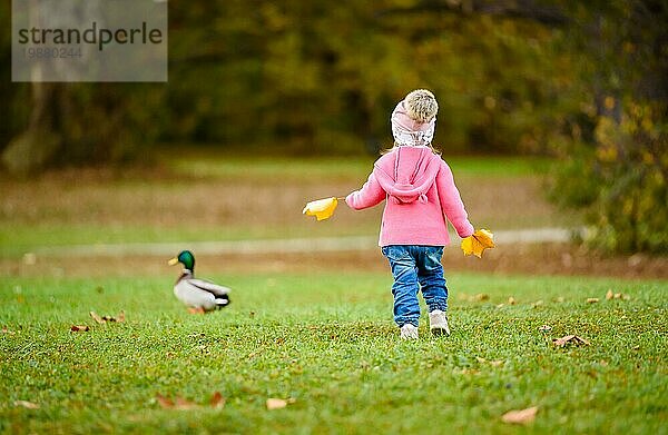 Porträt der bezaubernden Baby Mädchen hält gelbe Blätter und jagt wilde Ente im Herbst Park. Baby in der Natur Konzept