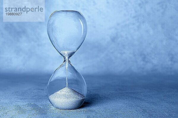 Konzept Die Zeit läuft ab . Eine Sanduhr mit durchfallendem Sand  mit Kopierraum  getönt in der Farbe des Jahres  blau