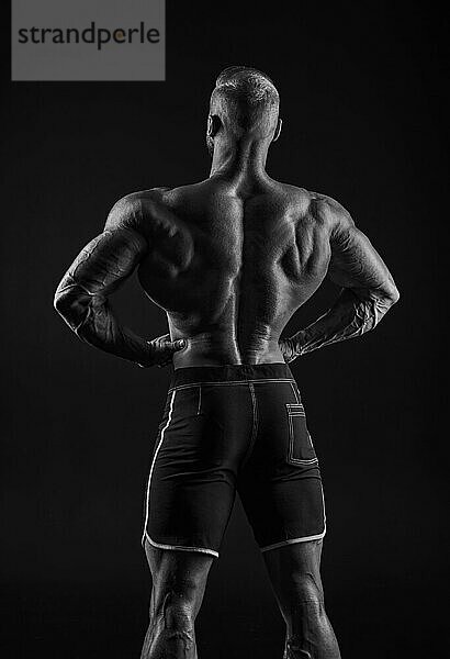 Silhouette eines kräftigen Bodybuilders. Blick von hinten. Selbstbewusster junger Fitnesssportler mit kräftigem Körper und perfekten Bauchmuskeln. Schwarz Weiß Fotografie. Dramatisches Licht