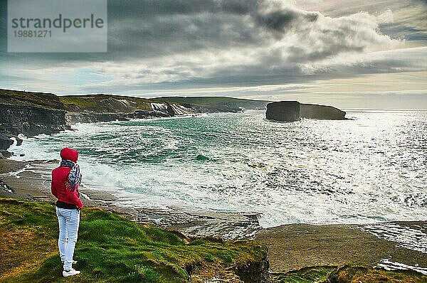 Frau beobachtet stürmisches Meer Der Kilkee Cliff Walk ist eine landschaftlich reizvolle  2 bis 3 Stunden dauernde (8 km) moderate Rundwanderung entlang der Kilkee Cliffs  die am Diamond Rocks Café  Pollock Holes Parkplatz  beginnt