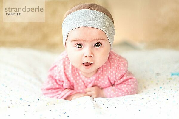 Adorable Baby Mädchen mit grauen Stirnband Blick in Richtung Kamera und lächelnd. Gesundheit Konzept. 6 Monate altes Baby