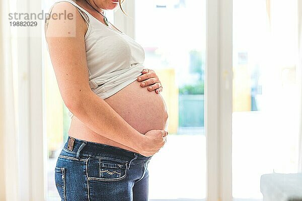 Glückliche kaukasische schwangere Mutter  die ihren nackten Bauch berührt  Blue Jeans  Nahaufnahme