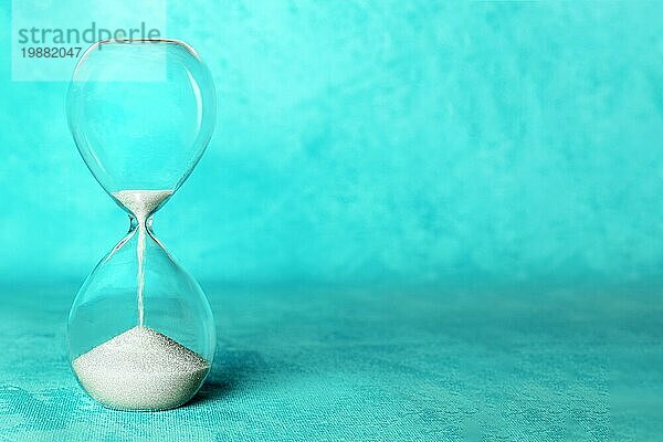 Zeit Konzept. Eine Sanduhr mit Sand fallen durch  auf einem leuchtend blaün Hintergrund mit Kopie Raum
