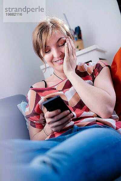Blondes attraktives Mädchen liegt auf dem Sofa und schreibt SMS mit ihrem Freund