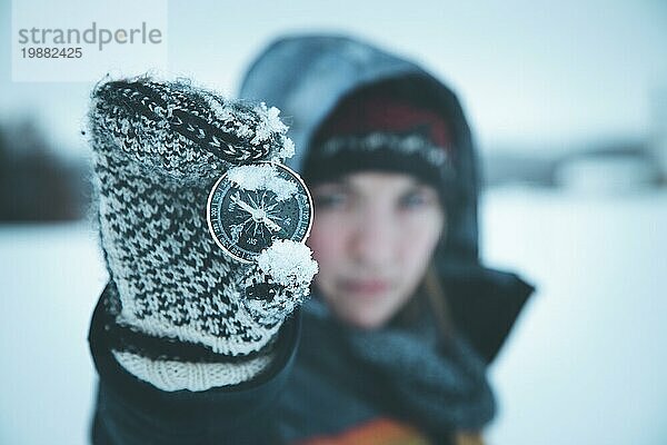 Junge Frau hält einen Kompass hoch. Winterzeit  Handschuhe und Kapuze