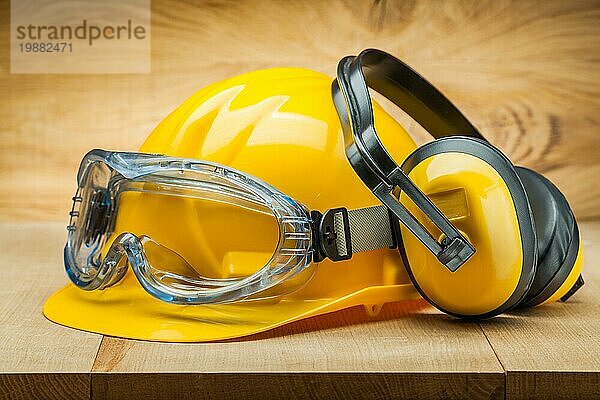 Sicherheit der Arbeit. Bau Sicherheit Werkzeuge. gelben Helm blaue Schutzbrille und Kopfhörer auf Holz Hintergrund