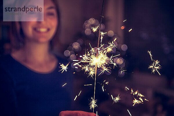 Lächelndes Mädchen hält eine Wunderkerze in der Hand  innen  Lichter im Hintergrund