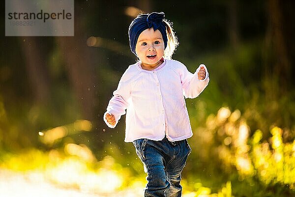 2 Jahre altes Baby Mädchen läuft im Wald in Richtung Kamera. mit glücklichen Ausdruck auf ihrem Gesicht. Baby in der Natur Konzept